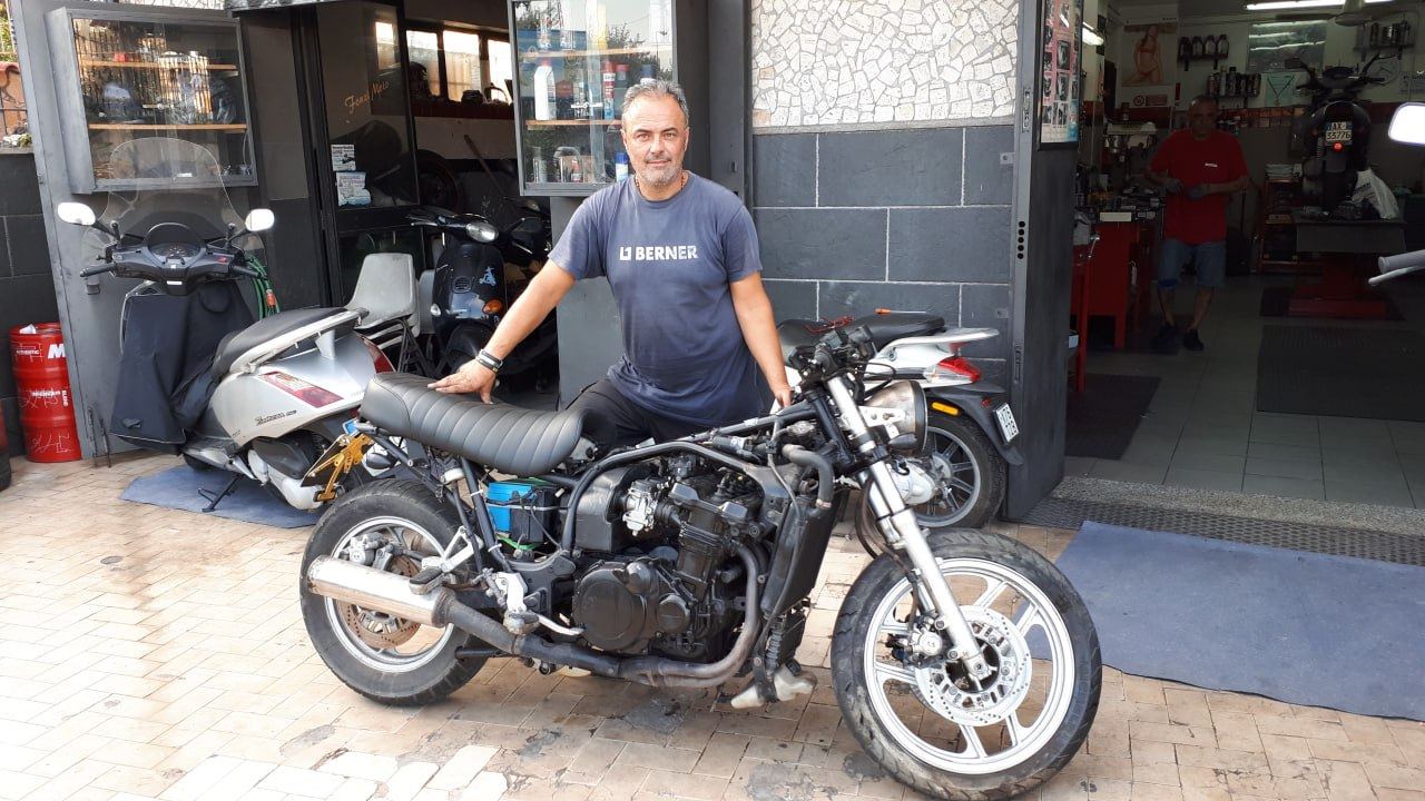 Meccanico dietro una moto in stile cafe racer davanti all'officina