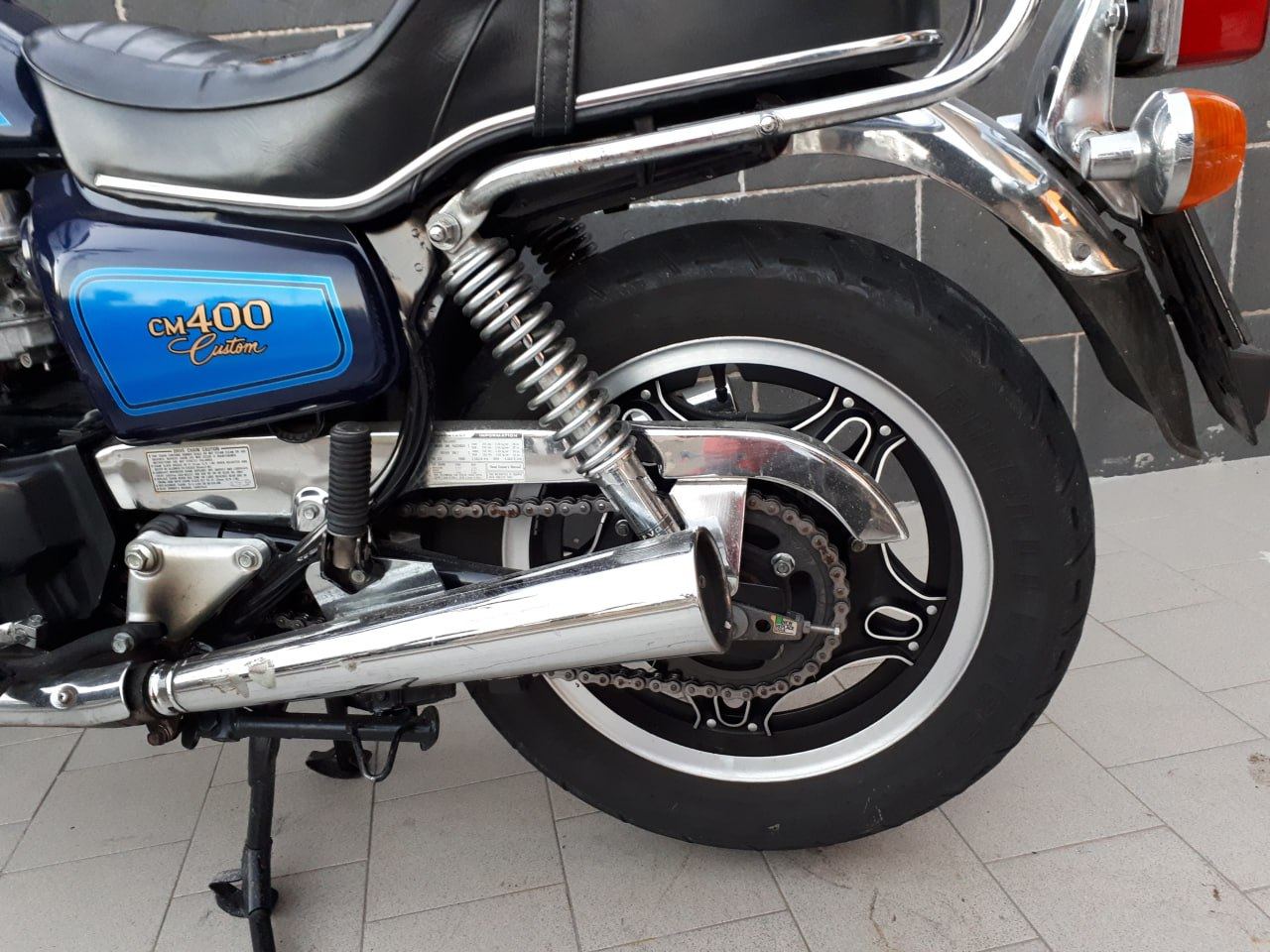 Dettaglio di scarico cromato, forcellone e ruota posteriore di una moto d'epoca