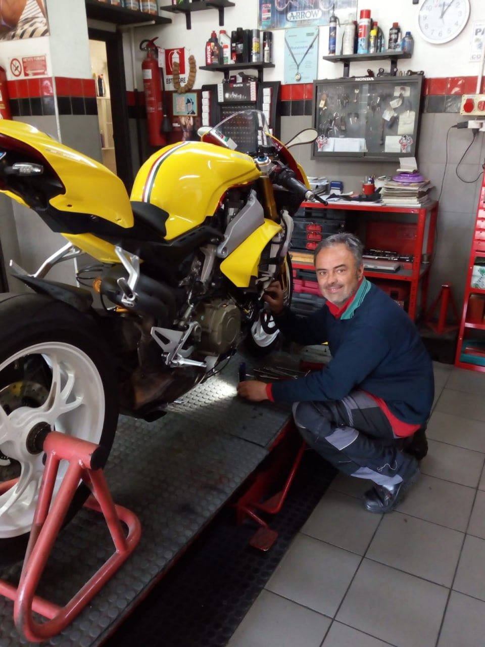 Meccanico al lavoro accanto a una moto sportiva gialla sul ponte